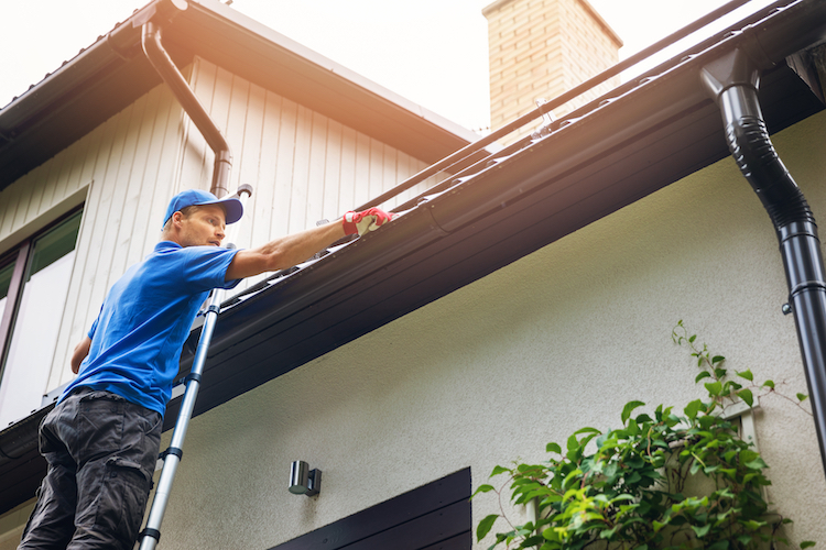 Man on Ladder Cleaning Gutters | K-Guard Heartland