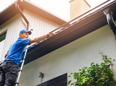 Man on Ladder Cleaning Gutters | K-Guard Heartland