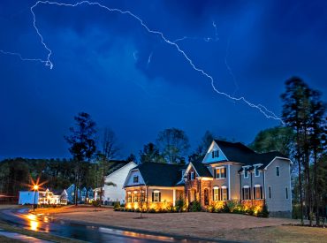 A bolt of lightning illuminates the night sky over a residential neighborhood.