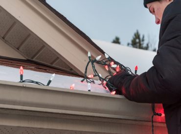 Man Standing on Ladder Hanging Festive Lights