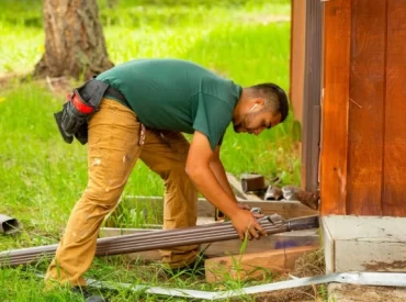 professional-gutter-installation-repair Technician installing rain gutters on the side of a wooden building.